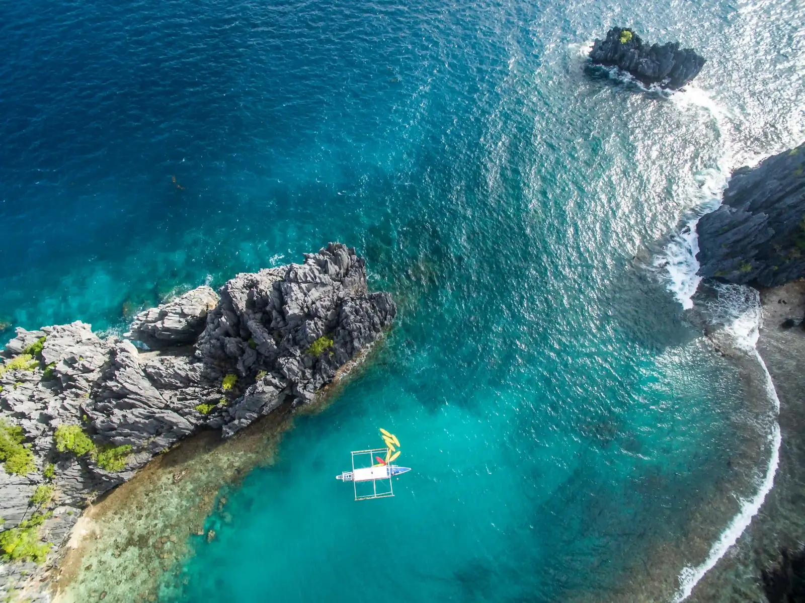 Tour boat with kayaks anchored in turquoise water beneath limestone rocks on El Nido's Tour C